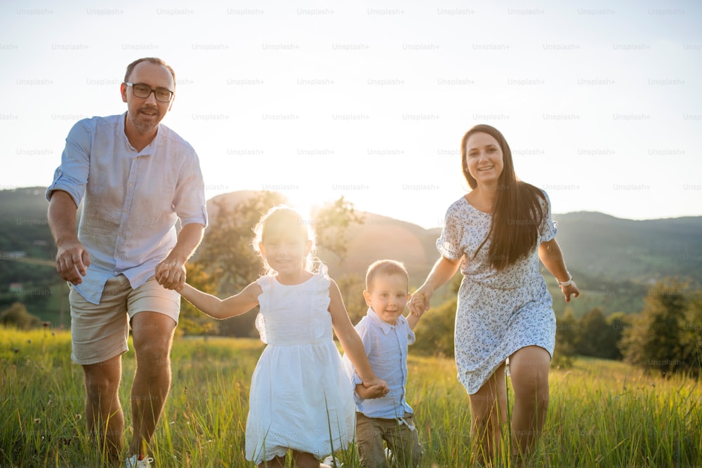 Happy young family with two small children running on meadow outdoors at sunset.