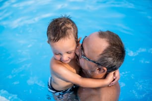 屋外のプールで小さな息子を抱く父親の上面図。