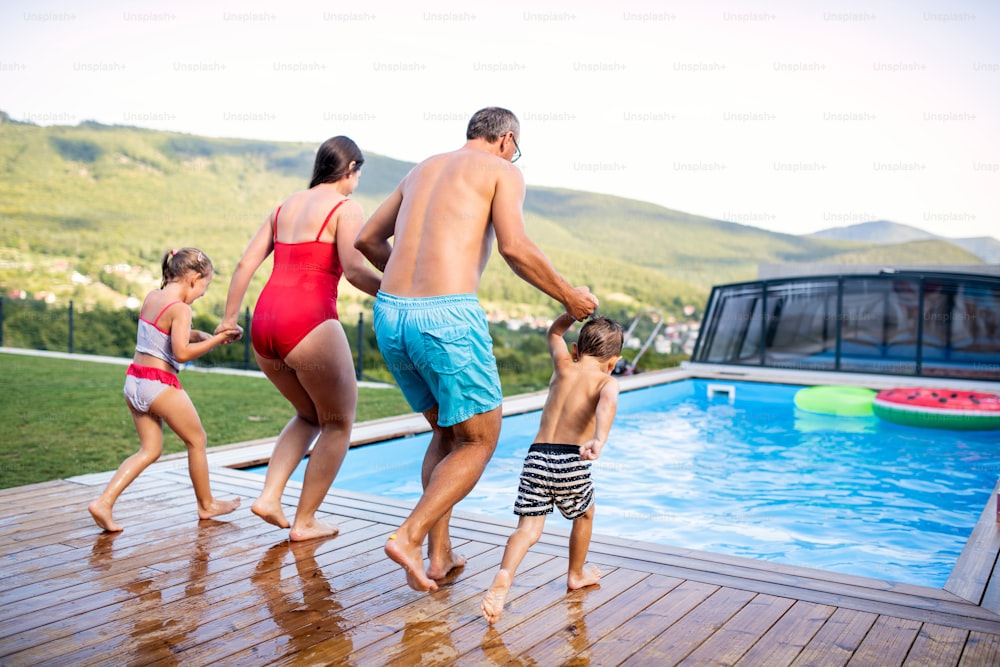Rear view of family with two small children by swimming pool outdoors, holding hands.
