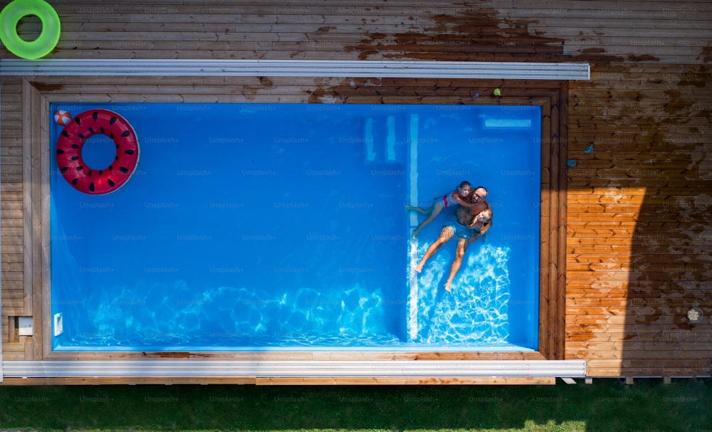 An aerial view of father with small children sitting in swimming pool outdoors.