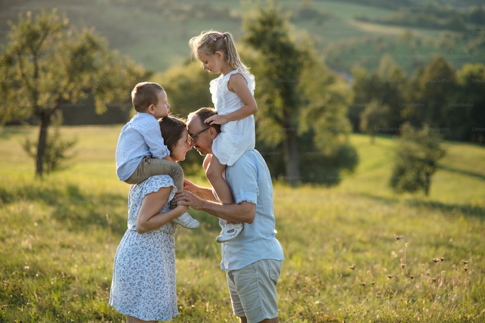 Familia joven y feliz con dos niños pequeños de pie en el prado al aire libre al atardecer.