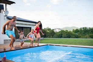 Familia joven con dos niños pequeños junto a la piscina al aire libre, tomados de la mano. Espacio de copia.