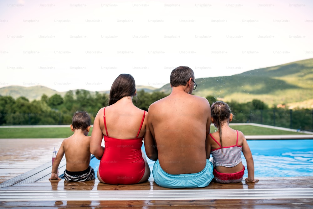 Rear view of family with two small children sitting by swimming pool outdoors.