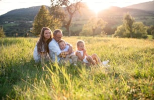 Familia joven y feliz con dos niños pequeños sentados en el prado al aire libre al atardecer.