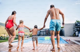 Rear view of family with two small children by swimming pool outdoors, holding hands.