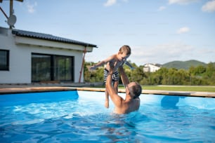 Un padre con un figlio piccolo felice che gioca in piscina all'aperto.