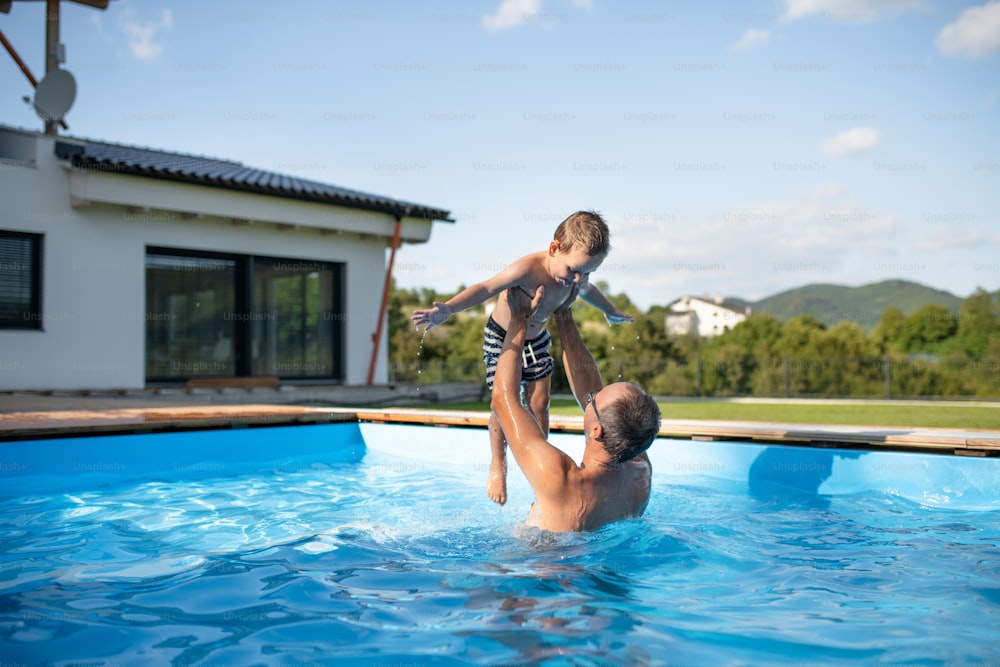 A father with happy small son playing in swimming pool outdoors.