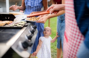 Midsection of multigeneration family outdoors on garden barbecue, grilling and talking.