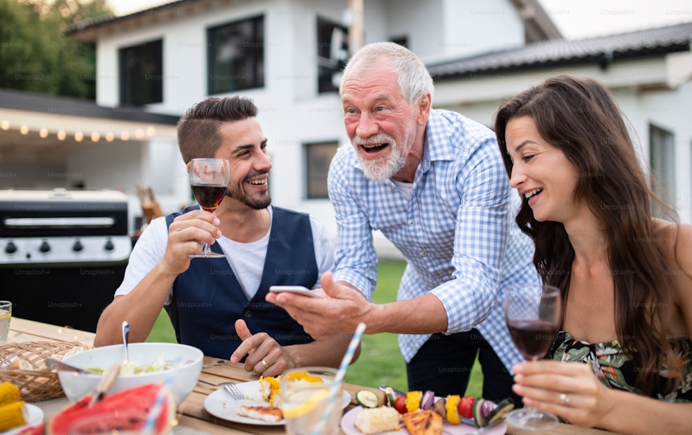 Un portrait de personnes à l’extérieur sur un barbecue de jardin familial, à l’aide d’un smartphone.