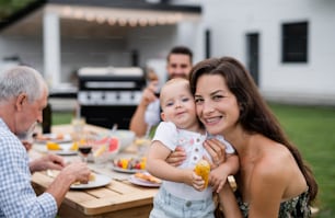 A portrait of extended family sitting at table outdoors on garden barbecue.