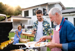 A portrait of multigeneration family outdoors on garden barbecue, grilling.