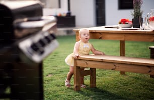Cute small girl standing outdoors on family garden barbecue.
