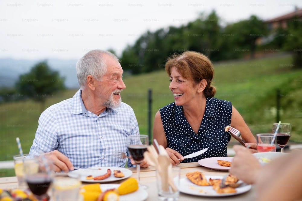 Senior couple sitting a t the table outdoors on family garden barbecue, eating.