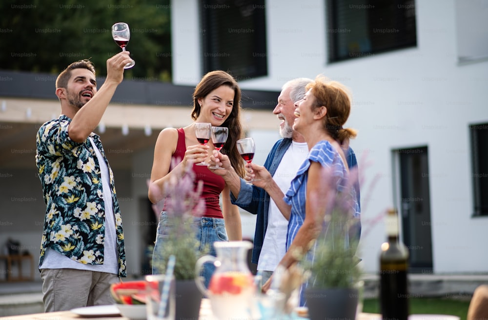 Portrait of people with wine outdoors on family garden barbecue, clinking glasses.