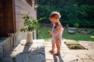 A cute toddler girl standing outdoors in front of house in summer. Copy space.