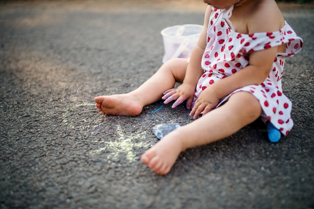 Midsection of unrecognizable toddler girl outdoors in countryside, chalk drawing on road.