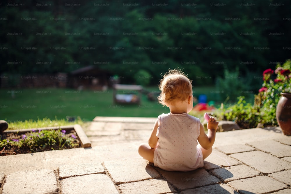 Una vista posteriore della bambina seduta all'aperto sul patio in estate, disegno di gesso.