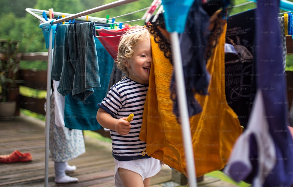 Dos niños pequeños felices parados al aire libre en una terraza en verano, jugando con la percha de secado de ropa.