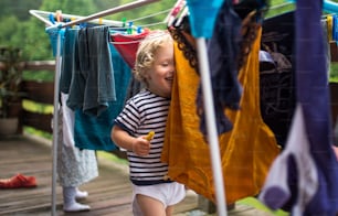 Two happy toddler children standing outdoors on a terrace in summer, playing with clothes drying hanger.