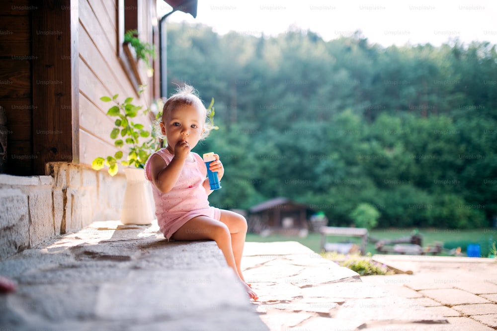 A cute toddler girl sitting outdoors in front of house in summer. Copy space.