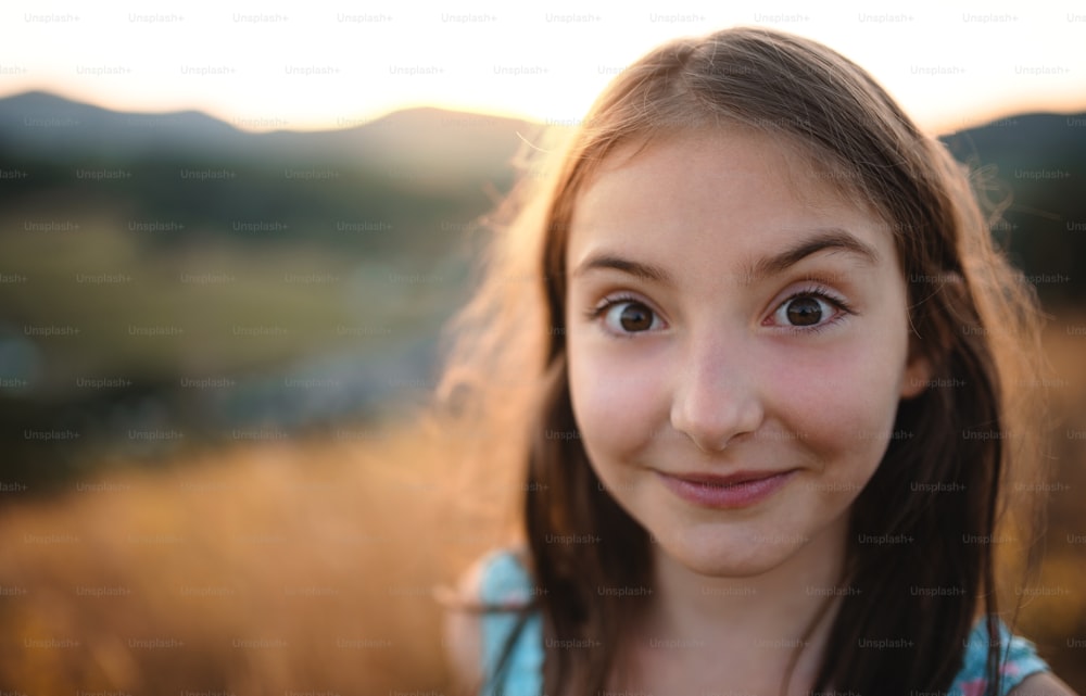 Um retrato headshot de menina pequena na natureza, olhando para a câmera.