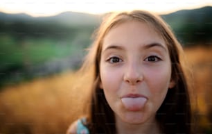 A headshot portrait of small girl in in nature, sticking out tongue.