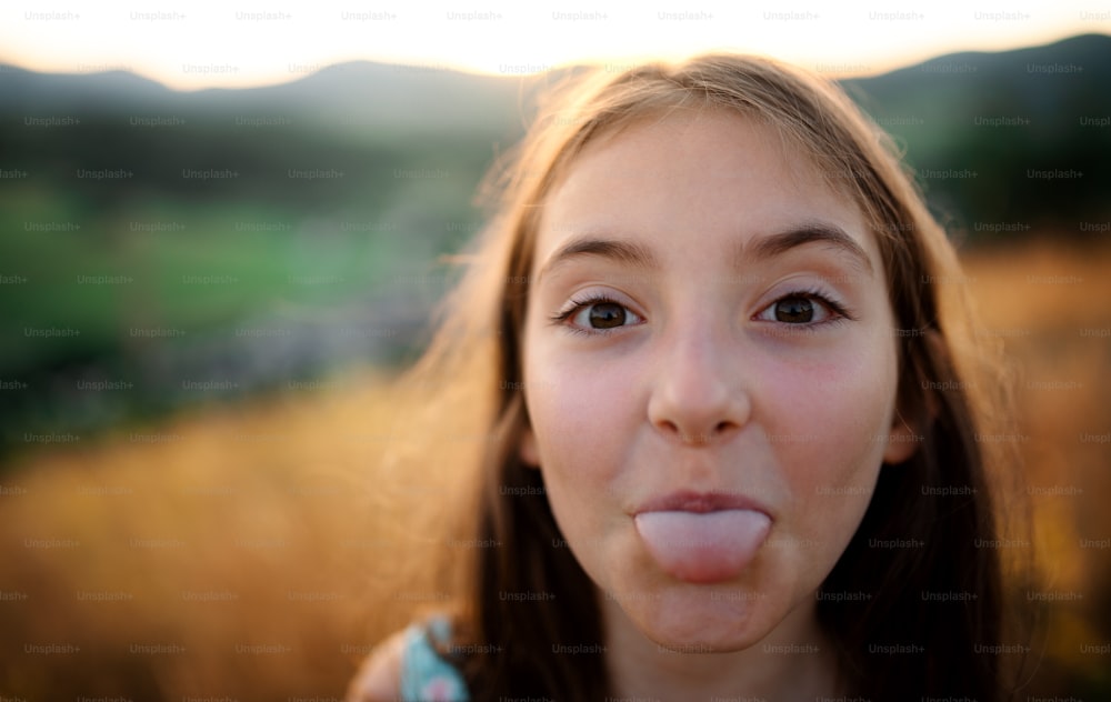 A headshot portrait of small girl in in nature, sticking out tongue.