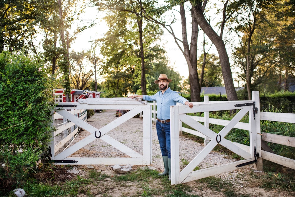 Ein Porträt eines reifen Bauern, der im Freien auf dem Familienbauernhof spazieren geht und das Tor öffnet.