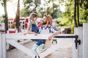 Ein Porträt des Vaters mit kleiner Tochter im Freien auf dem Bauernhof der Familie, der am Holztor steht.