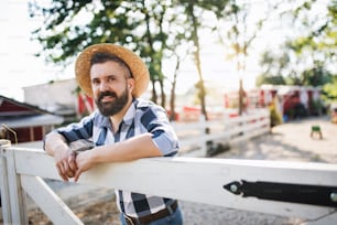 A portrait of mature man farmer with hat standing outdoors on family farm.