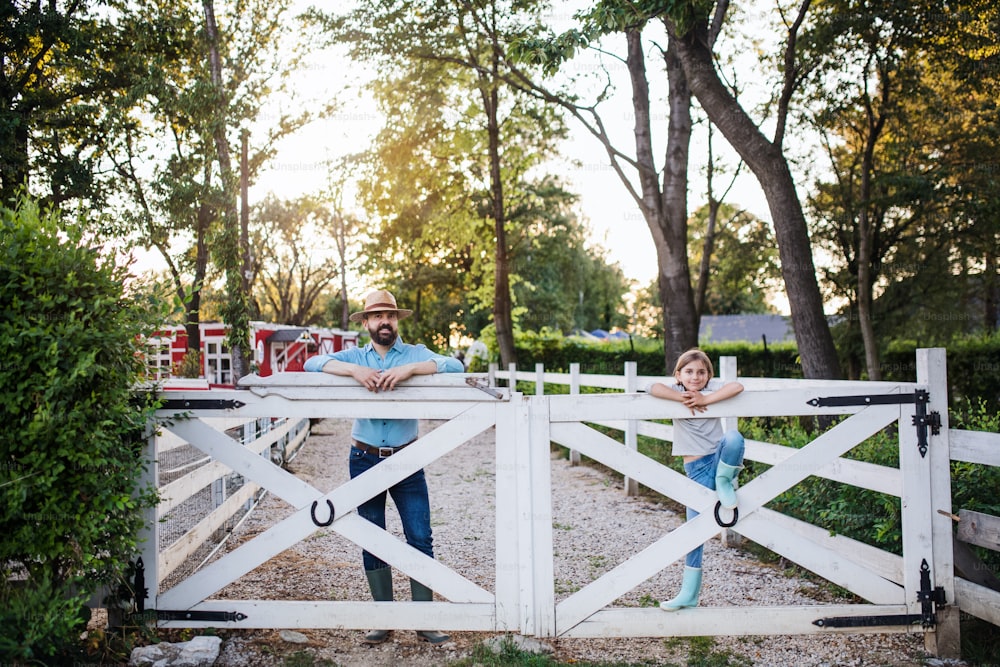 A portrait of father with small daughter outdoors on family farm, looking at camera.