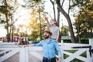 A portrait of father with small daughter outdoors on family farm, looking at camera.