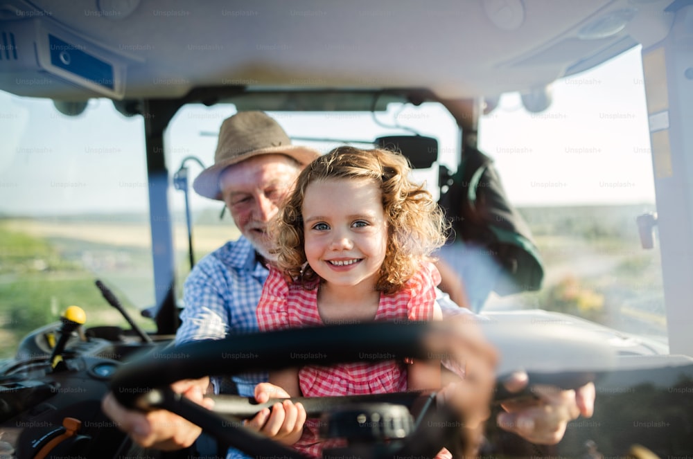 A senior farmer with small granddaughter sitting in tractor, driving.