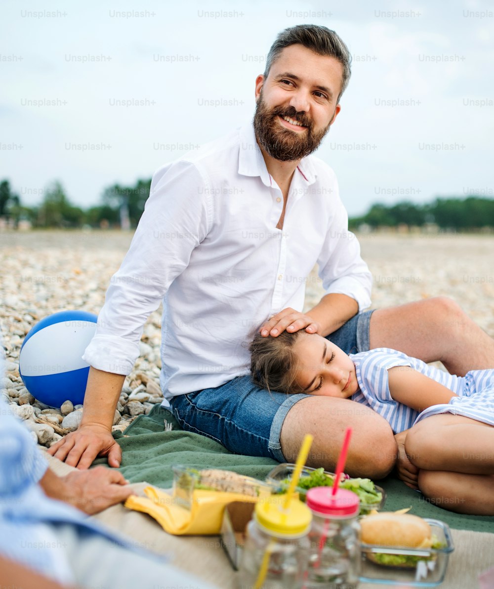 Mature father with tired daughter on a holiday by the lake, having picnic.