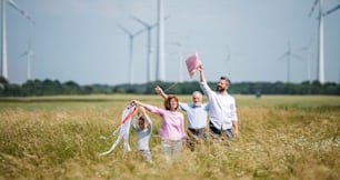 Front view of multigeneration family standing on field on wind farm, playing with kite.