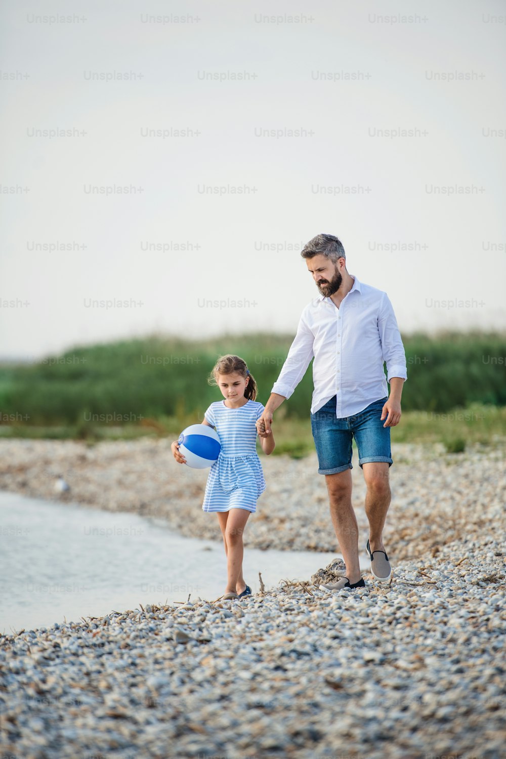 Un padre maduro y una hija pequeña en unas vacaciones caminando por el lago o el mar.