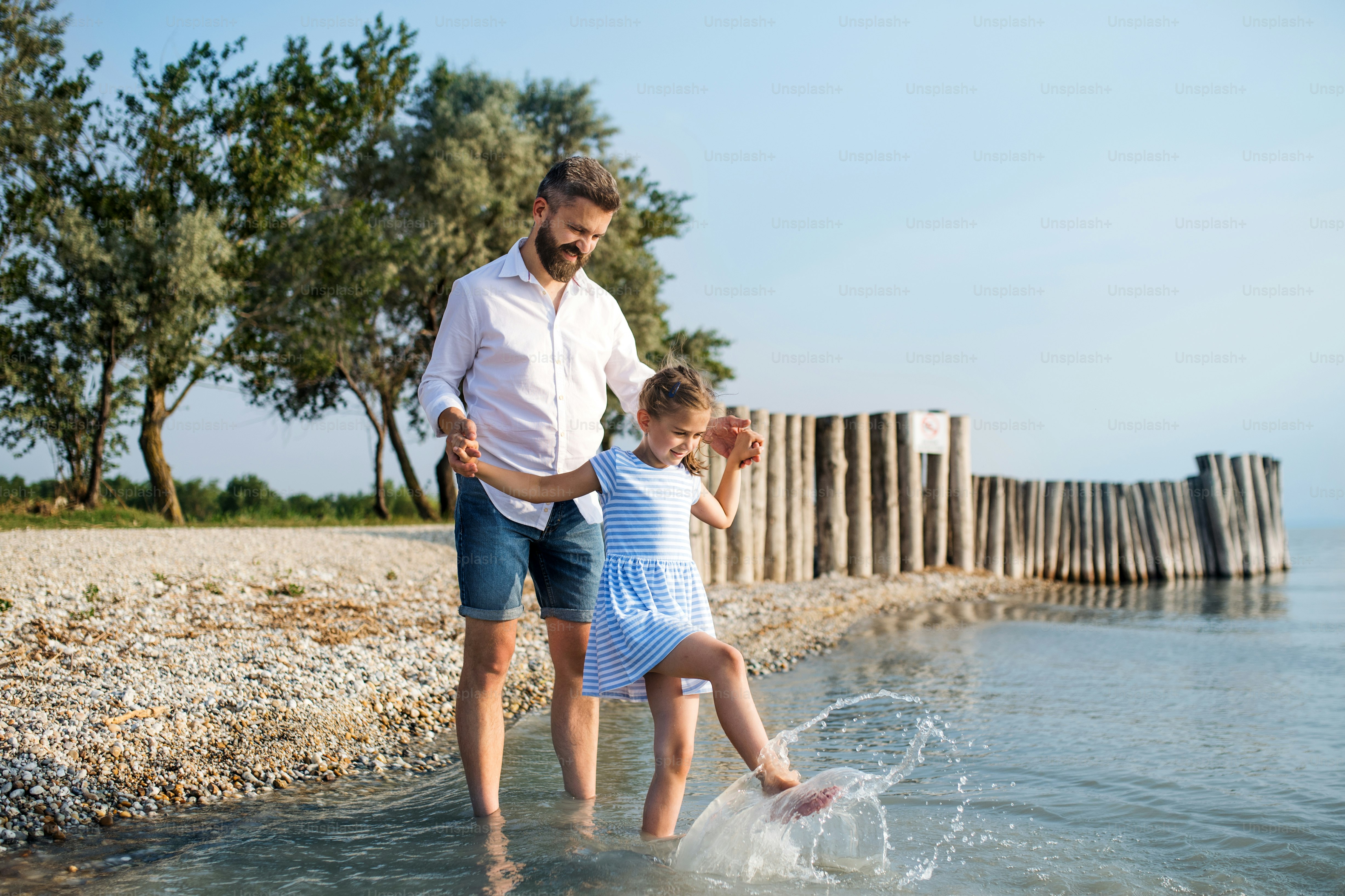 Ein reifer Vater und eine kleine Tochter im Urlaub, spielen am See oder am Meer und gehen barfuß