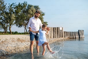 Un padre maduro y una hija pequeña en unas vacaciones jugando junto al lago o al mar, caminando descalzos.