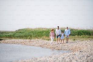 Une famille multigénérationnelle en vacances marchant au bord du lac, se tenant la main.