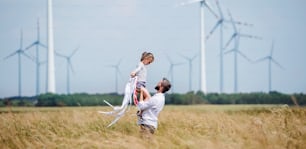 어린 딸을 둔 성숙한 아버지가 풍력 발전 단지의 들판에 서서 놀고 있다.