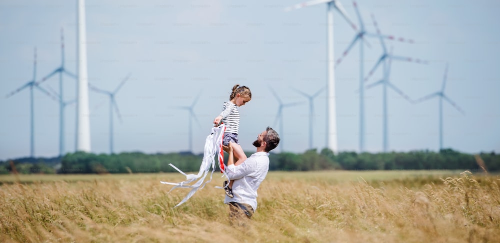 Padre maturo con la figlia piccola in piedi sul campo del parco eolico, giocando.