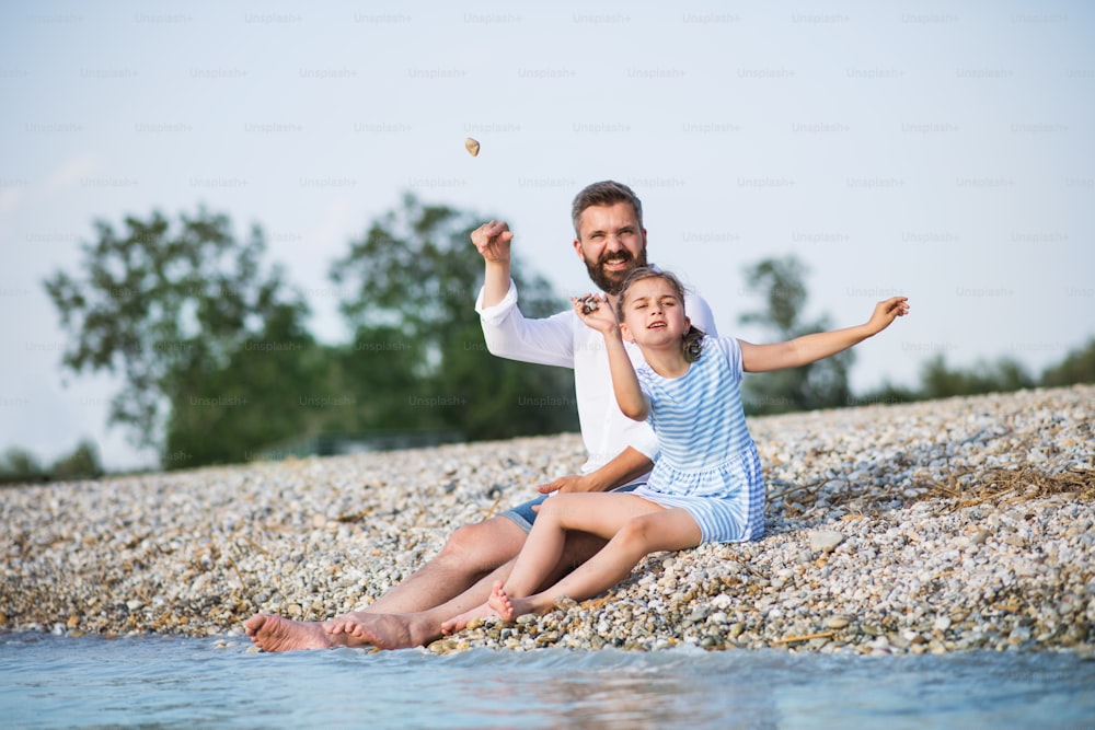 Padre e piccola figlia in vacanza seduti al lago o al mare.