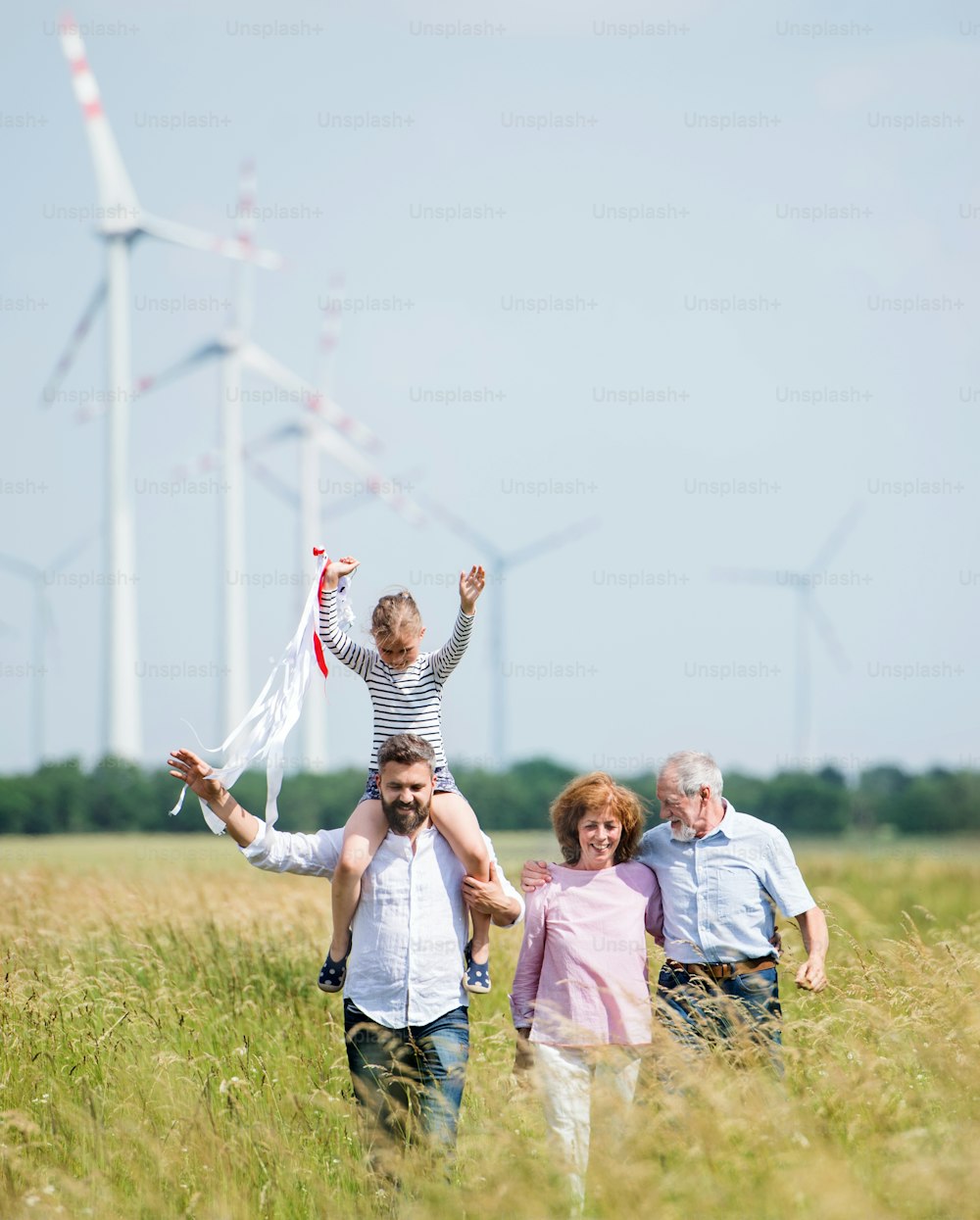 Eine Vorderansicht einer Mehrgenerationenfamilie, die auf dem Feld eines Windparks spazieren geht.
