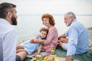 Una familia multigeneracional de vacaciones junto al lago, haciendo un picnic.