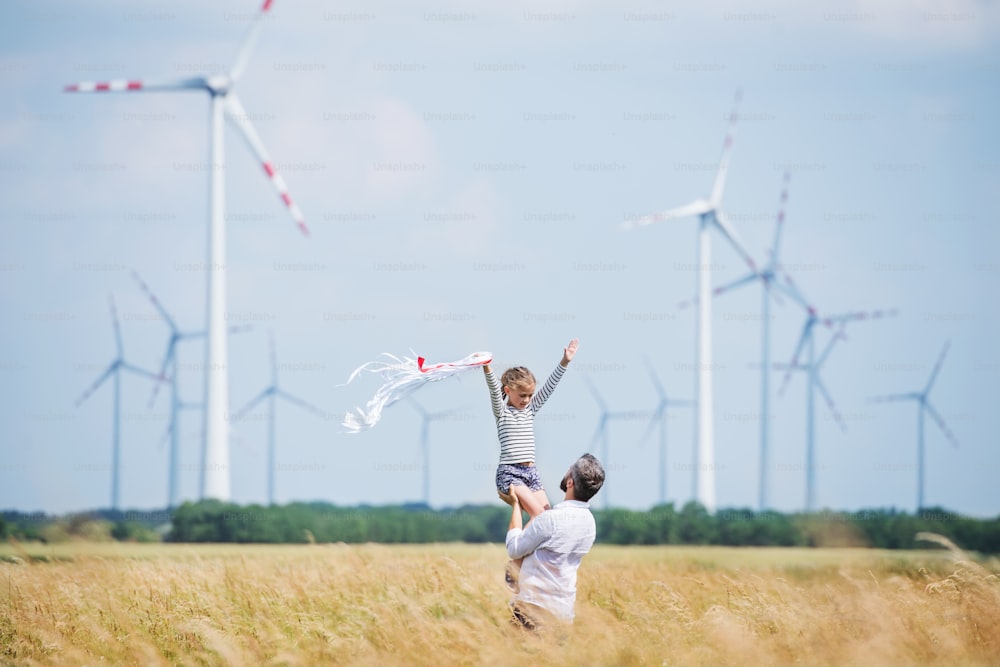 Padre maturo con la figlia piccola in piedi sul campo del parco eolico, giocando.