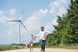 Un padre maturo con una figlia piccola sul campo del parco eolico, in esecuzione.