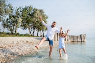 A mature father and small daughter on a holiday playing by the lake or sea, walking barefoot.