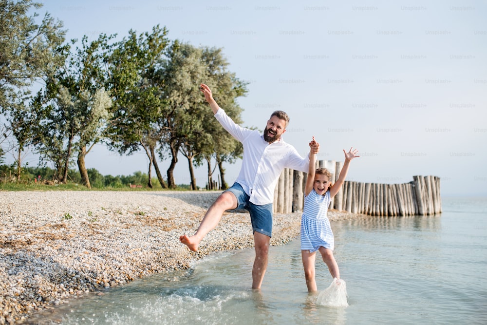 A mature father and small daughter on a holiday playing by the lake or sea, walking barefoot.