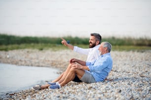 Senior father and mature son sitting by the lake, talking. Copy space.