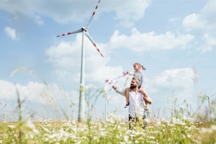 Padre maduro con una hija pequeña caminando en el campo en un parque eólico, dándole un paseo a cuestas.